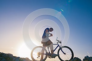 Strong fit male mountain biker performing stunts on rocky terrain on a sunset while wearing a blue shirt and riding a blue bike