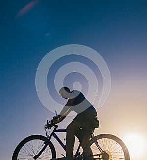 Strong fit male mountain biker performing stunts on rocky terrain on a sunset while wearing a blue shirt and riding a blue bike