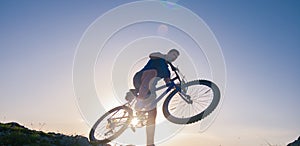 Strong fit male mountain biker performing stunts on rocky terrain on a sunset while wearing a blue shirt and riding a blue bike