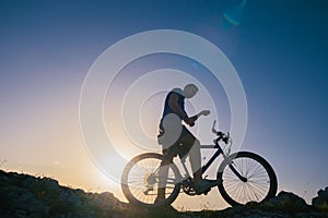 Strong fit male mountain biker performing stunts on rocky terrain on a sunset while wearing a blue shirt and riding a blue bike