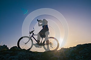 Strong fit male mountain biker performing stunts on rocky terrain on a sunset while wearing a blue shirt and riding a blue bike