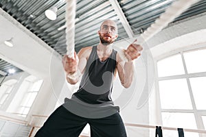 Strong fitness sportsman using training ropes for cross workout at gym