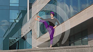 Strong flexible young girl yogi muslim islamic woman stands background of city building doing yoga workout tree pose