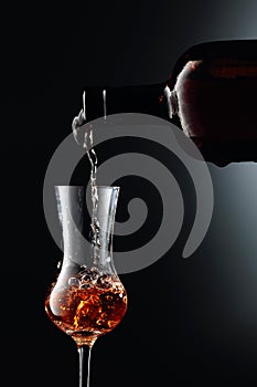 Strong golden alcoholic drink from the antique bottle being poured into a  glass