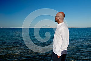 Strong handsome beautiful man in black fashion sunglasses, white shirt enjoys vacation trip at sea takes suntan at sunny summer