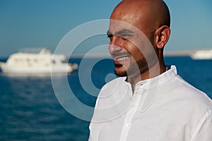 Strong handsome beautiful man in black fashion sunglasses, white shirt enjoys vacation trip at sea takes suntan at sunny summer