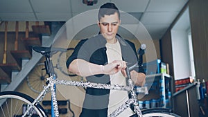 Strong handsome man skilled mechanic is concentrated on repairing handlebar of broken bicycle in his small workshop