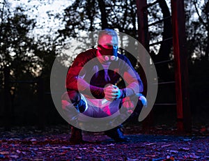 Strong handsome and muscular squatting slav taking a break from hard street workout, man in squatting position