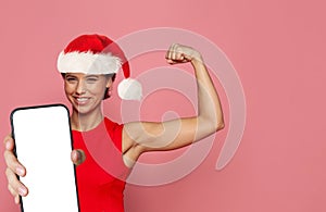 Strong happy Christmas woman in red Santa had showing smartphone with empty white screen display against colorful pink studio wall