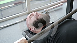 Strong heavyweight athlete thoroughly doing barbell exercise with strained face