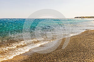 Strong katabatic wind pushes Aegean sea waves back from shore under clear sky, creating striking reverse flow effect on water. photo