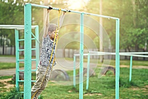 Strong kid doing exercises with a fitness elastic band on sports ground