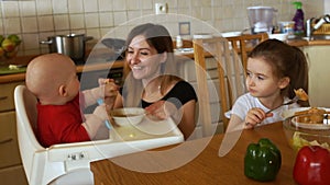 A strong kid eats in a highchair in the kitchen. Mom can`t take the spoon from him. Healthy Nutrition for Kids