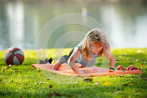 Strong kid push up exercise on the roll mat in the park outdoor. Athletic boy is pushing up on the green grass.