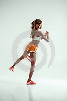 Strong legs. Full length of young african woman with beautiful body doing exercises with resistance band in studio