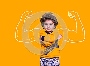 Strong little confident child showing bicep muscles. Funny curly hispanic boy isolated on yellow background. Strength