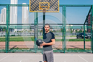 Strong male basketball player preparing for a basketball game on a sunny day wearing a black tee and grey shorts