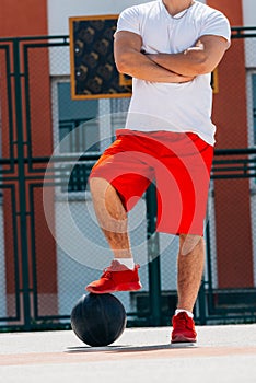 Strong male basketball player preparing for a basketball game on a sunny day wearing a black tee and grey shorts