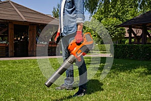 Strong male gardener cleaning backyard garden lawn, while using gasoline cordless leaf blower.