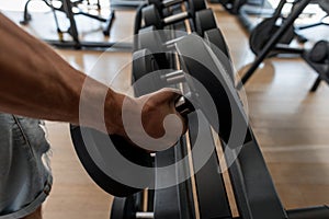 Strong male hand lifting a dumbbell in a sports studio. Athletic young man trains in the gym. Close-up of a man`s hand