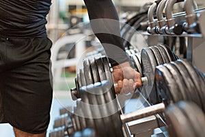 Strong male hand lifting a dumbbell in a sports studio. Athletic young man trains in the gym.