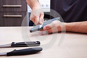 Strong male hands sharpen a kitchen metal knife with a grindstone. Home household knife sharpening