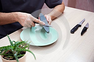 Strong male hands sharpen a kitchen metal knife with a grindstone. Home household knife sharpening