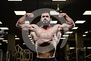 Strong male physique concept of muscular young bearded handsome man showing muscles biceps in fitness gym