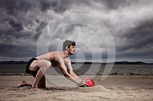 Strong male with red ball on the beach