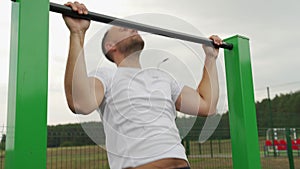 Strong man from behind doing pull ups on horizontal bar. Mans fitness at the stadium