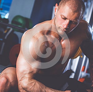 Strong man, bodybuilder exercising with dumbbells in a gym