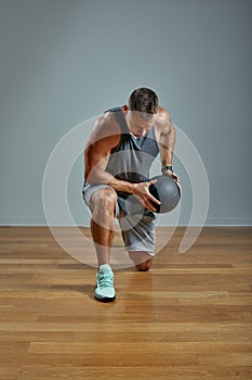 Strong man doing exercise with med ball. Photo of man perfect physique on grey background. Strength and motivation.