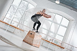 Strong man doing jumping exercises over box at a cross training style gym