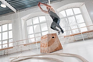 Strong man doing jumping exercises over box at a cross training style gym