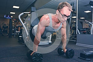 Strong man doing push-ups exercises on dumbbells