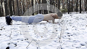 Strong man doing push ups on snow at winter forest. Sportsman exercising at nature. Young guy training outdoor. Muscular