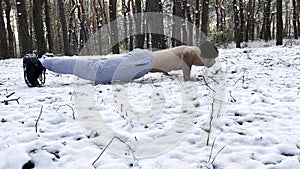 Strong man doing push ups on snow at winter forest. Sportsman exercising at nature. Young guy training outdoor. Muscular