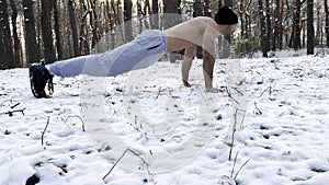 Strong man doing push ups on snow at winter forest. Sportsman exercising at nature. Young guy training outdoor. Muscular