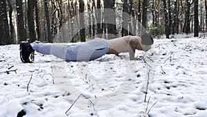 Strong man doing push ups on snow at winter forest. Sportsman exercising at nature. Young guy training outdoor. Muscular