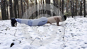 Strong man doing push ups on snow at winter forest. Sportsman exercising at nature. Young guy training outdoor. Muscular