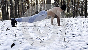 Strong man doing push ups on snow at winter forest. Sportsman exercising at nature. Young guy training outdoor. Muscular