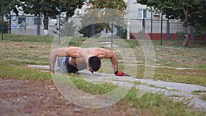 Strong man doing push ups at sports ground. Young sportsman exercising outdoor. Muscular athlete showing hard and