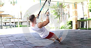 Strong man doing push-ups with TRX on street platform