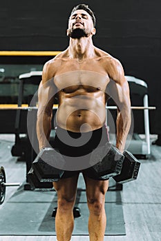 Strong man holding dumbbells in a gym with satisfaction expression