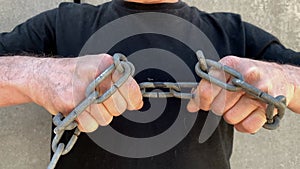 Strong man holds thick iron chains in his hands, yanks them, tries to break the steel, the concept of strength, fetters, bondage,