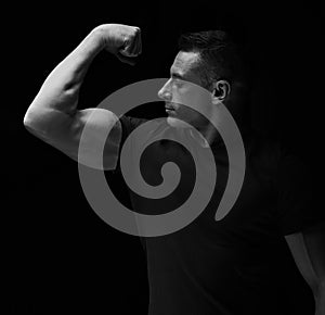 Strong man looking and showing her biceps arm on dark black background