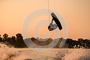 strong man making trick in jump time with wakeboard on sunset sky background.