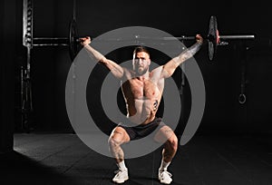 Strong man performing overhead squat pressing barbell up, full length shot. Routine workout for physical and mental