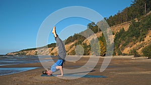 Strong man practicing difficult yoga pose on the beach