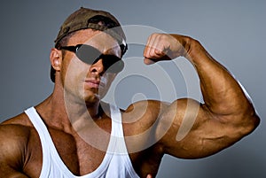 A strong man shows his muscles. Trained body. The gray background